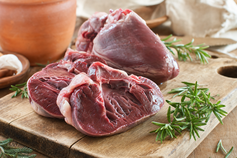 Raw lamb hearts sliced on a wooden board, a nutrient-dense organ meat for a dog's raw diet